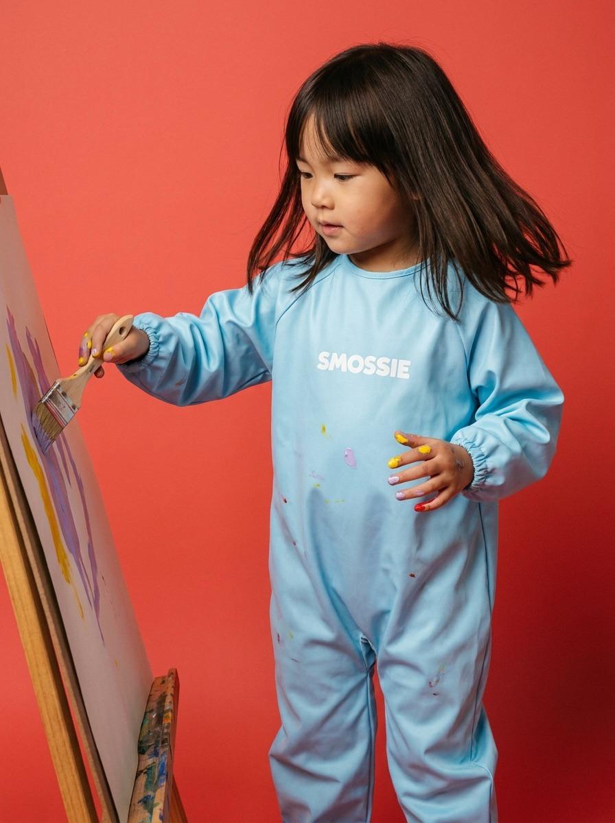 A child painting at an easel in a sky blue Smossie suit